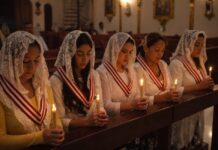 La Iglesia que vela cuando el mundo duerme Grupo de mujeres mexicanas en una iglesia, con velo blanco y velas encendidas, orando en silencio durante una vigilia de adoración eucarística nocturna.