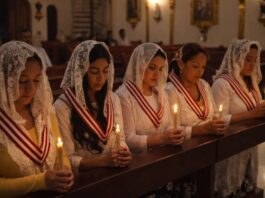 La Iglesia que vela cuando el mundo duerme Grupo de mujeres mexicanas en una iglesia, con velo blanco y velas encendidas, orando en silencio durante una vigilia de adoración eucarística nocturna.