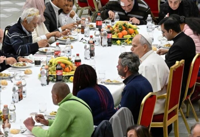 El Papa León XIV sentado a la mesa con personas pobres durante una comida comunitaria en el Vaticano.
