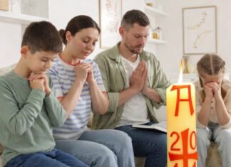 Domingo de Resurrección: el dia que la vida vence y la alegría se comparte Familia reunida en casa en actitud de oración, con un cirio pascual encendido en primer plano, símbolo de la Resurrección de Cristo.