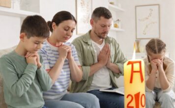 Domingo de Resurrección: el dia que la vida vence y la alegría se comparte Familia reunida en casa en actitud de oración, con un cirio pascual encendido en primer plano, símbolo de la Resurrección de Cristo.