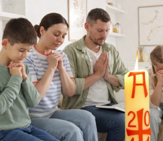 Domingo de Resurrección: el dia que la vida vence y la alegría se comparte Familia reunida en casa en actitud de oración, con un cirio pascual encendido en primer plano, símbolo de la Resurrección de Cristo.