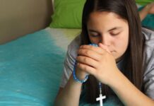 Las jaculatorias: pequeñas oraciones que mantienen el corazón cerca de Dios Manos entrelazadas en oración con un rosario, en un ambiente cálido y contemplativo que representa la espiritualidad cotidiana del católico.