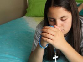 Las jaculatorias: pequeñas oraciones que mantienen el corazón cerca de Dios Manos entrelazadas en oración con un rosario, en un ambiente cálido y contemplativo que representa la espiritualidad cotidiana del católico.