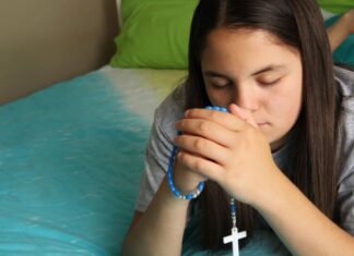 Las jaculatorias: pequeñas oraciones que mantienen el corazón cerca de Dios Manos entrelazadas en oración con un rosario, en un ambiente cálido y contemplativo que representa la espiritualidad cotidiana del católico.