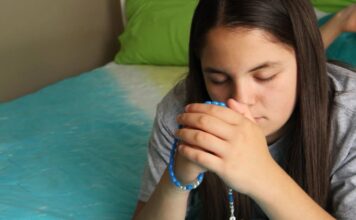 Las jaculatorias: pequeñas oraciones que mantienen el corazón cerca de Dios Manos entrelazadas en oración con un rosario, en un ambiente cálido y contemplativo que representa la espiritualidad cotidiana del católico.