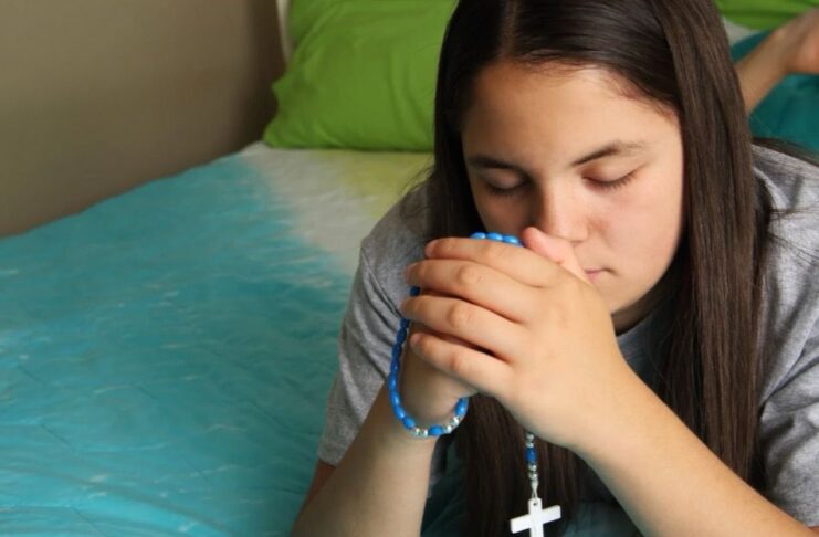 Las jaculatorias: pequeñas oraciones que mantienen el corazón cerca de Dios Manos entrelazadas en oración con un rosario, en un ambiente cálido y contemplativo que representa la espiritualidad cotidiana del católico.