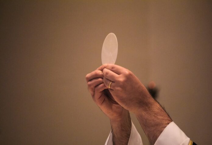 Corpus christi Sacerdote elevando una hostia consagrada durante la celebración de la Eucaristía, en un momento de adoración y recogimiento litúrgico.