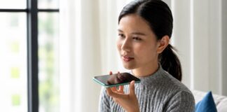 Inteligencia Artificial y pastoral juvenil: custodiar la humanidad en la era digital Joven sentada en una sala sosteniendo un teléfono móvil cerca de su rostro mientras utiliza una aplicación de inteligencia artificial por voz.