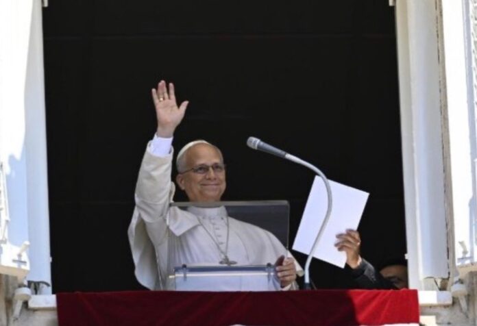 El Papa León XIV saluda con la mano desde la ventana del Palacio Apostólico durante el rezo del Ángelus, sosteniendo el texto de su mensaje.