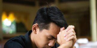 El examen de conciencia: una práctica olvidada que puede transformar nuestra vida Joven católico orando en silencio dentro de una iglesia, con las manos entrelazadas mientras realiza un examen de conciencia al finalizar el día.