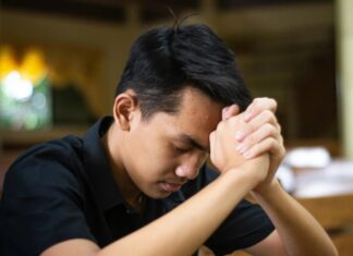 El examen de conciencia: una práctica olvidada que puede transformar nuestra vida Joven católico orando en silencio dentro de una iglesia, con las manos entrelazadas mientras realiza un examen de conciencia al finalizar el día.