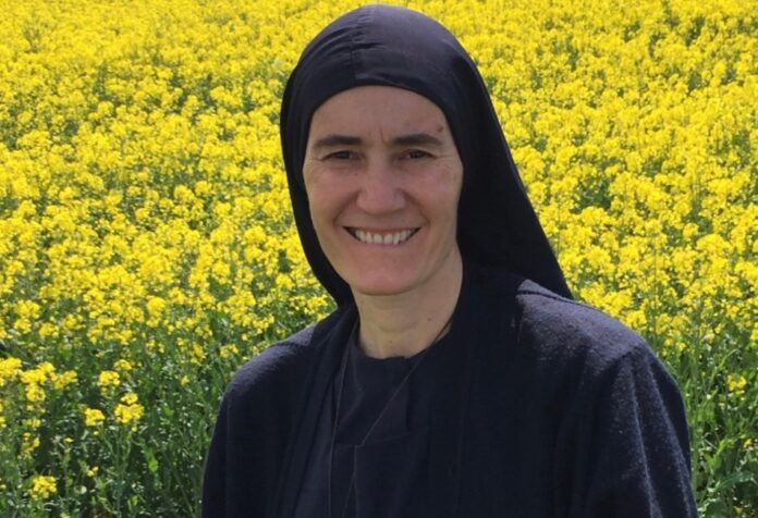 La Madre María Elena sonríe frente a un amplio campo de flores amarillas, vistiendo su hábito religioso y un crucifijo sobre el pecho