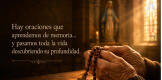¿Por qué rezamos el Ave María? Manos sostienen un rosario de madera dentro de una iglesia iluminada por la luz que entra por un vitral, mientras una imagen desenfocada de la Virgen María aparece al fondo.
