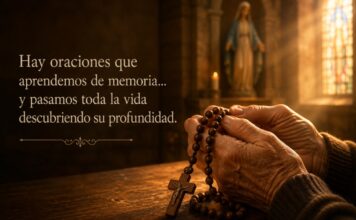 ¿Por qué rezamos el Ave María? Manos sostienen un rosario de madera dentro de una iglesia iluminada por la luz que entra por un vitral, mientras una imagen desenfocada de la Virgen María aparece al fondo.
