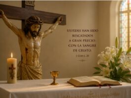 Julio y la Preciosísima Sangre de Cristo: una devoción que nos recuerda hasta dónde llega el amor de Dios Crucifijo sobre un altar con una Biblia abierta, un pequeño cáliz, un cirio encendido y lirios blancos, como representación de la devoción a la Preciosísima Sangre de Cristo durante el mes de julio.