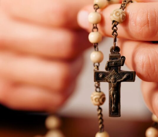 Rezar el Rosario por los difuntos: una oración de esperanza y amor Persona sosteniendo un rosario mientras ora por el eterno descanso de los fieles difuntos.
