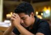 ¿Y si Dios sigue llamando? Joven en oración dentro de un templo católico, con las manos entrelazadas y la cabeza inclinada en actitud de discernimiento vocacional.