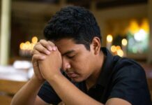 ¿Y si Dios sigue llamando? Joven en oración dentro de un templo católico, con las manos entrelazadas y la cabeza inclinada en actitud de discernimiento vocacional.