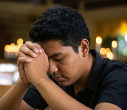 ¿Y si Dios sigue llamando? Joven en oración dentro de un templo católico, con las manos entrelazadas y la cabeza inclinada en actitud de discernimiento vocacional.